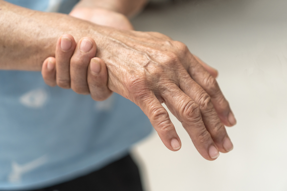 Elderly person grasping hand due to autoimmune condition.


